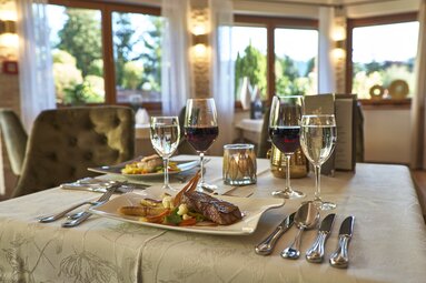 Auf einem gedeckten Tisch steht ein Hauptgericht sowie zwei Gläser Wein und Wasser. | © Bodenmais Tourismus & Marketing GmbH