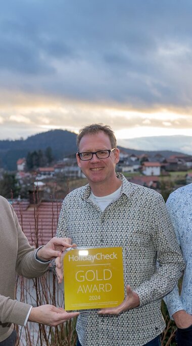 Vier Männer stehen auf einer Terrasse mit Ausblick und halten eine gelbe Auszeichnung, auf der HolidayCheck Gold Award steht. | © Bodenmais Tourismus & Marketing GmbH