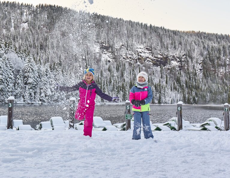 Zwei Mädchen mit neonfarbenen Skianzügen stehen am Ufer des verschneiten Arbersees und werfen Schnee in die Höhe. | © Bodenmais Tourismus & Marketing GmbH