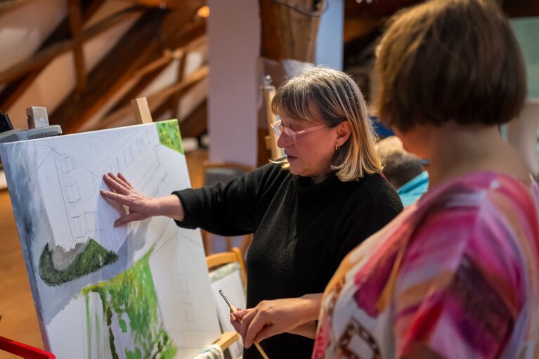 Kuratorin Kalina Svetlinski steht am Gemälde einer Teilnehmerin des Kunstseminars und erklärt etwas. | © Bodenmais Tourismus & Marketing GmbH