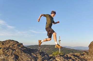 Ein Trailrunner springt auf einem Berggipfel von einem Stein zum anderen. | © Bodenmais Tourismus & Marketing GmbH