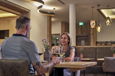 Ein Paar sitzt sich im Genussrestaurant Das FRANZ an einem Tisch gegenüber. Die Frau lacht den Mann an. Am Tisch stehen Weingläser. | © Bodenmais Tourismus & Marketing GmbH