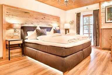 Im Schlafzimmer einer Ferienwohnung steht ein großes, graues Boxspringbett, welches unten beleuchtet ist. | © Bodenmais Tourismus & Marketing GmbH