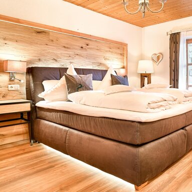 Im Schlafzimmer einer Ferienwohnung steht ein großes, graues Boxspringbett, welches unten beleuchtet ist. | © Bodenmais Tourismus & Marketing GmbH