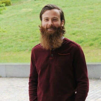 Ein Mann mit langem, braunen Bart steht vor einer Grünfläche und lächelt in die Kamera. Er trägt einen weinroten Pullover.  | © Markt Bodenmais