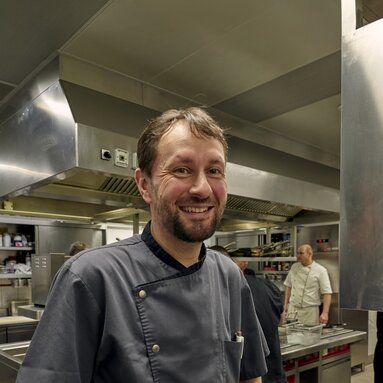 In der Küche steht ein Mann und lacht in die Kamera. | © Bodenmais Tourismus & Marketing GmbH