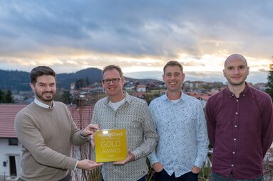 Vier Männer stehen auf einer Terrasse mit Ausblick und halten eine gelbe Auszeichnung, auf der HolidayCheck Gold Award steht. | © Bodenmais Tourismus & Marketing GmbH