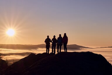 Vier Personen stehen auf einem Gipfel. Man sieht nur die schwarzen Umrissen. Vor ihnensteht die Sonne tief. | © Bodenmais Tourismus & Marketing GmbH