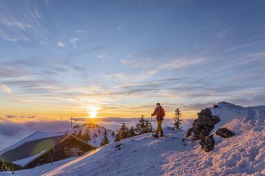 Ein Wanderer mit Schneeschuhen läuft oberhalb der Arberschutzhütte Richtung Gipfel. Die niedrig stehende Sonne taucht den winterlichen Berg in warmes Licht. | © Bodenmais Tourismus & Marketing GmbH