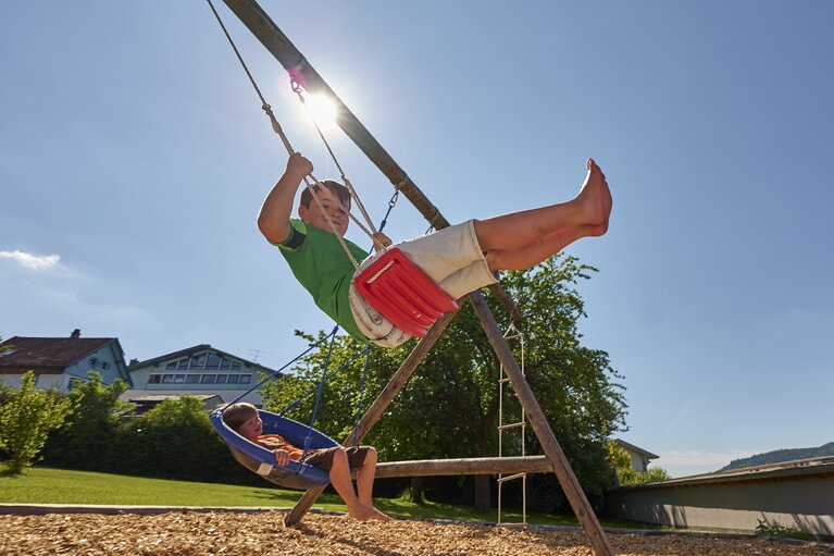 Ein Junge schaukelt hoch auf einer Schaukel. Ein anderer Junge liegt in einer Hängeschaukel. | © Bodenmais Tourismus & Marketing GmbH