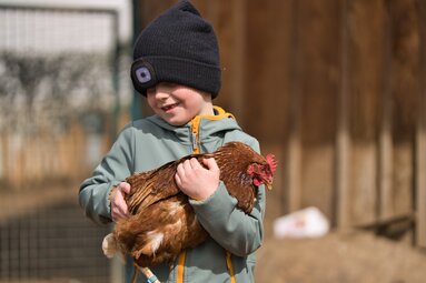 Ein Kind mit Mütze trägt ein Huhn. | © Bodenmais Tourismus & Marketing GmbH