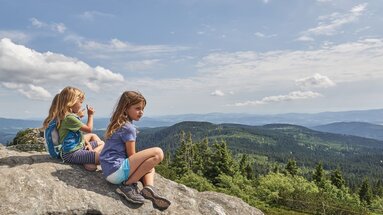 Drei Mädchen sitzen auf einem Felsen und schauen in das bergige Umland, den Bayerischen Wald | © Bodenmais Tourismus & Marketing GmbH