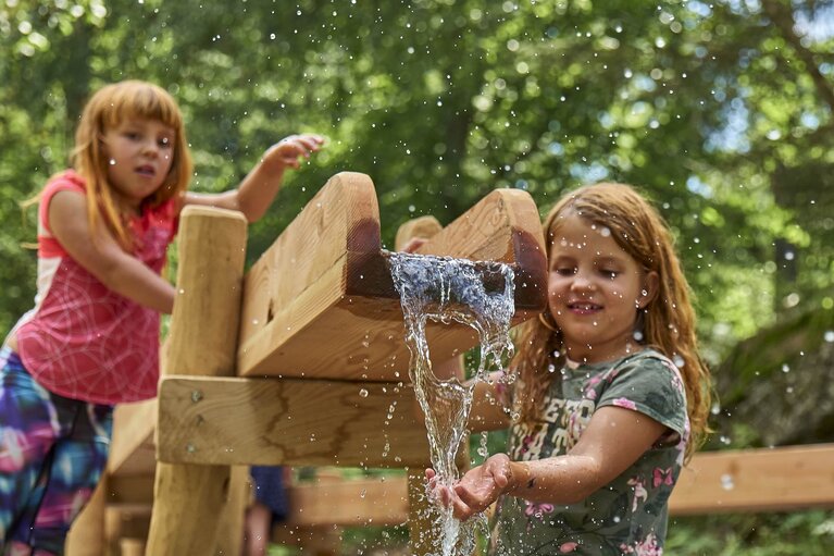 Zwei Mädchen spielen mit dem Wasser, das aus einer Holzrinne fließt | © Bodenmais Tourismus & Marketing GmbH