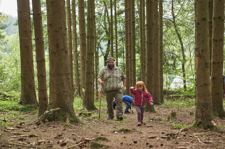 Der Woid Woife, ein großer, kräftiger Mann mit Filzhut, kariertem Hemd und Stock, wandert zusammen mit mehreren Kindern durch den Wald. | © Bodenmais Tourismus & Marketing GmbH