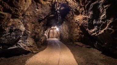 Ein Weg im Bergwerk führt zu einer hölzerne Tür. Der Tunnel ist grob in den Fels geschlagen. | © Bodenmais Tourismus & Marketing GmbH