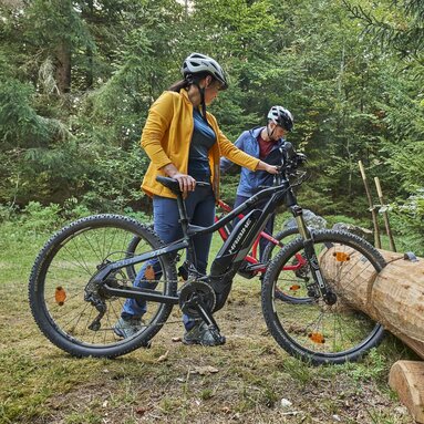 Eine Frau und ein Mann stellen ihre Fahrräder an einem Fahrradständer ab, der aus einem Baumstamm gefertigt wurde. | © Bodenmais Tourismus & Marketing GmbH