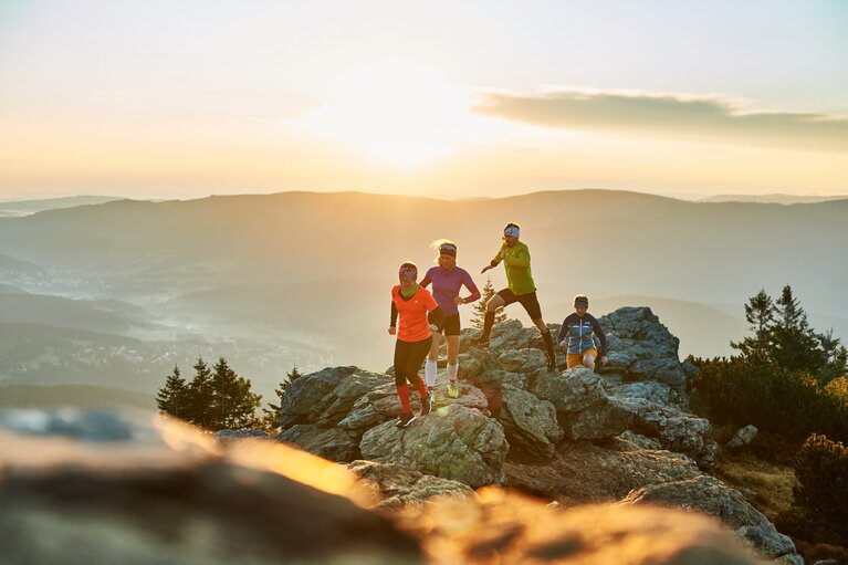 Vier Trailläufer laufen auf einem Berggipfel. Hinter ihnen geht die Sonne unter unter färbst alles in oranges Licht. | © Bodenmais Tourismus & Marketing GmbH