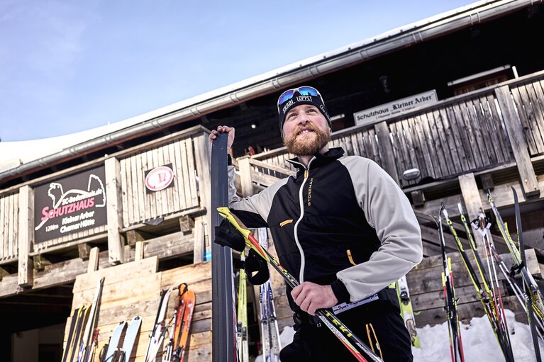 Ein Langläufer steht mit seinen Skiern in der Hand vor dem Schutzhaus Kleiner Arber Chamer Hütte | © Bodenmais Tourismus & Marketing GmbH