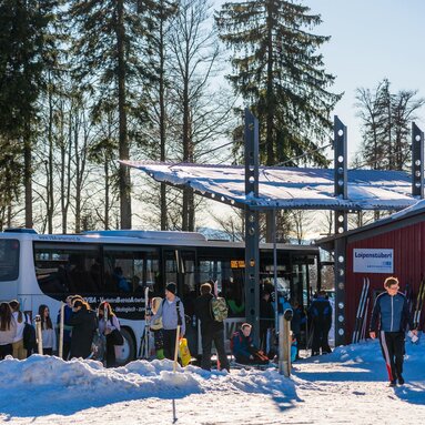 Am Langlaufzentrum Bretterschachten hält neben dem Loipenstüberl der Skibus. Viele Langläufer stehen bereits an der Haltestelle, | © Bodenmais Tourismus & Marketing GmbH