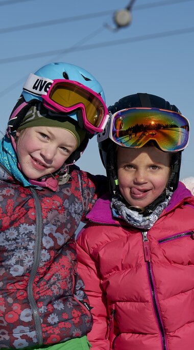 Zwei Mädchen in Skianorak und Skihelm posieren auf einer Skipiste für ein Foto. | © Bodenmais Tourismus & Marketing GmbH