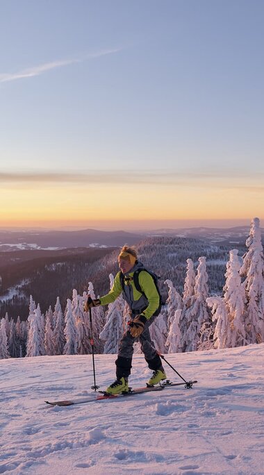 Ein Mann geht auf seinen Tourenski über eine freie, beschneite Fläche auf einem Berg. Die Sonne geht unter und hüllt alles in ein warmes Licht. | © Bodenmais Tourismus & Marketing GmbH