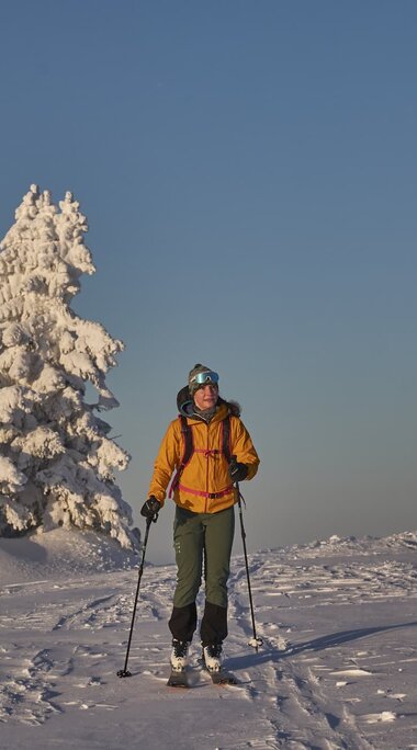 Eine Skitourengeherin läuft auf einem Berg über den Schnee. Nur vereinzelt stehen schneebedeckte Nadelbäume. | © Bodenmais Tourismus & Marketing GmbH