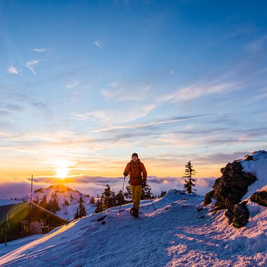 Ein Schneeschuhwanderer befindet sich am Großen Arber. Hinter ihm geht die Sonne unter und im Tal liegt der Nebel. | © Bodenmais Tourismus & Marketing GmbH