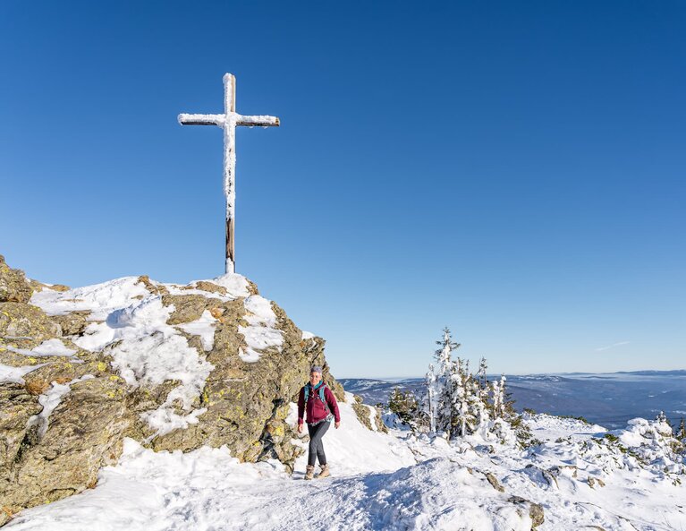 Eine Frau wandert unterhalb des verschneiten Gipfelkreuzes vom Großen Arber die letzte Meter hinauf. | © Bodenmais Tourismus & Marketing GmbH