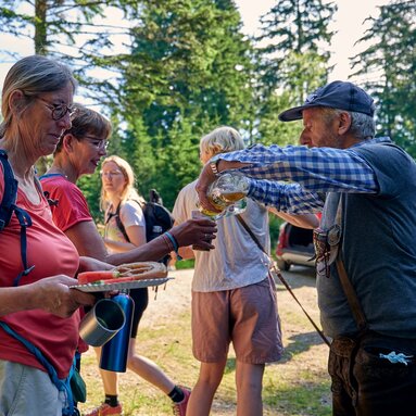 Eine Frau hält einen vollen Teller in der Hand eine weitere Frau lässt sich ihren Becher mit Apfelschorle füllen. | © Bodenmais Tourismus & Marketing GmbH