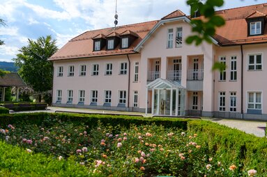 Über Rosen und den Brunnenhof hinweg blickt man auf das rosa, dreistöckige Neue Rathaus. | © jokumaxx design