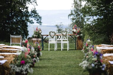 Auf einer Wiese auf der GutsAlm Harlachberg wurde eine Trauung vorbereitet. Als Sitze dienen den Gästen Heuballen, die mit Blumen geschmückt sind. | © Maiores Photographie