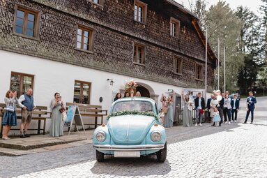 Ein Brautpaar fährt in einem hellblauen Oldtimer vom Alten Rathaus davon. Die Braut hält ihren Strauß aus dem Caprio und die Gäste jubeln. | © Lisa Bauer Photography