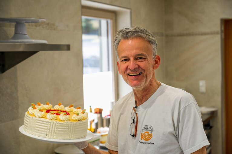 Ein Bäcker steht in der Backstube und hält eine Torte hoch. | © Bodenmais Tourismus & Marketing GmbH