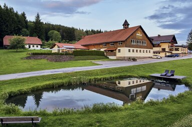 Über einen kleinen Teich mit Liegen hinweg blickt man auf das Hotel Böhmhof. | © Bodenmais Tourismus & Marketing GmbH