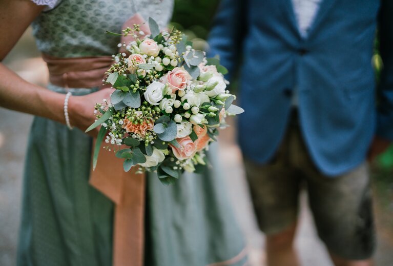 Ein Brautstrauß in weiß, grün und rosé Tönen wird in die Kamera gehalten | © Fouquet Production