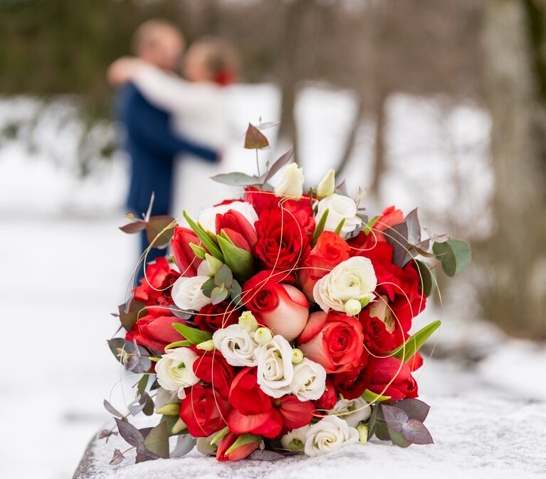 Auf Schnee liegt ein Brautstrauß aus weißen und roten Rosen sowie Tulpen. | © jokumaxx design