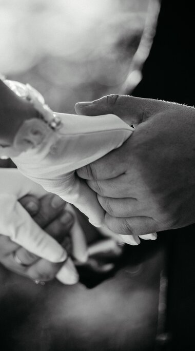 Ein Mann im Anzug und eine Frau mit kurzen weißen Handschuhe halten die Hände. | © Fouquet Production