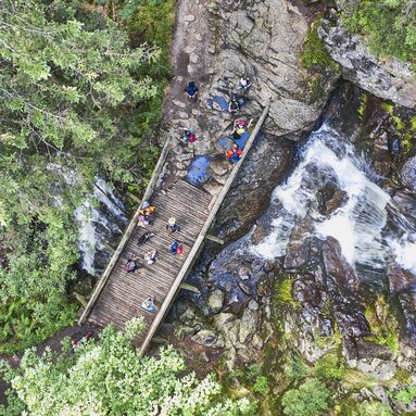 Mehrere Wanderer überqueren eine Holzbrücke über einen Wasserfall, der in Stufen verläuft. | © Bodenmais Tourismus & Marketing GmbH