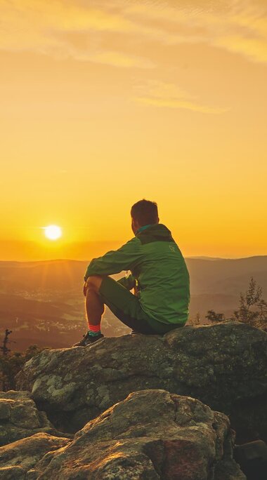 Ein Mann sitzt am Gipfel des großen Arbers und schaut zur aufgehenden Sonne. | © Bodenmais Tourismus & Marketing GmbH