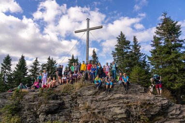 Eine große Gruppe Wanderer posiert am Gipfelkreuz des Kleinen Arbers für ein Gruppenfoto. | © Bodenmais Tourismus & Marketing GmbH
