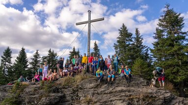 Eine große Gruppe Wanderer posiert am Gipfelkreuz des Kleinen Arbers für ein Gruppenfoto. | © Bodenmais Tourismus & Marketing GmbH