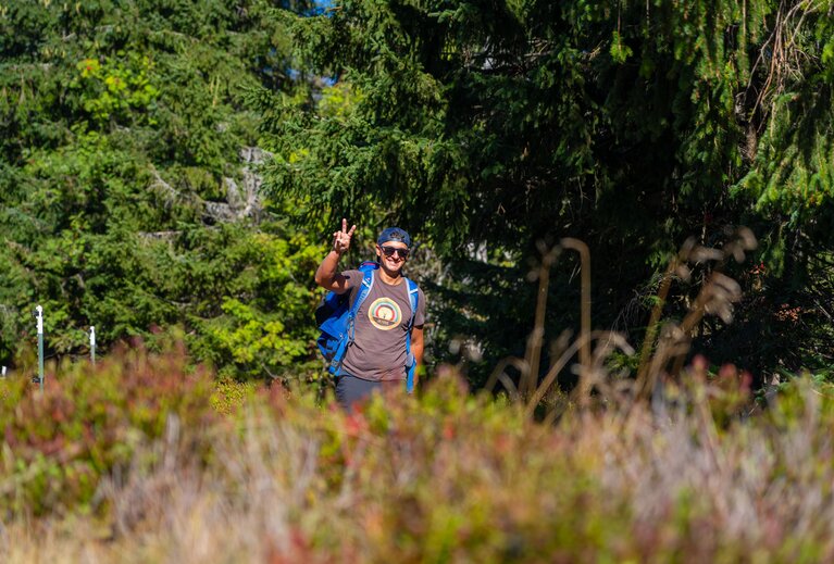 Durch die Heidelbeersträucher fotografiert  sieht man einen Wanderer, der Peace zeigt. | © Bodenmais Tourismus & Marketing GmbH
