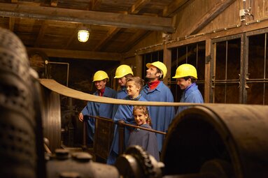 Eine Gruppe aus vier Erwachsenen und zwei Kindern bestaunt einen alten Kompressor im Bergwerk. | © Bodenmais Tourismus & Marketing GmbH