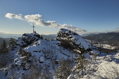 Von etwas weiter weg sieht man zwei Personen am verschneiten Gipfel des Silberbergs sitzen. | © Bodenmais Tourismus & Marketing GmbH