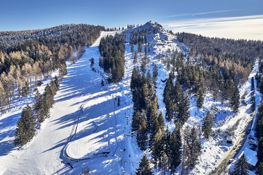 An einem sonnigen Wintertag blickt man aus der Vogelperspektive auf die Skipiste und den Gipfel des Silberbergs. | © Bodenmais Tourismus & Marketing GmbH