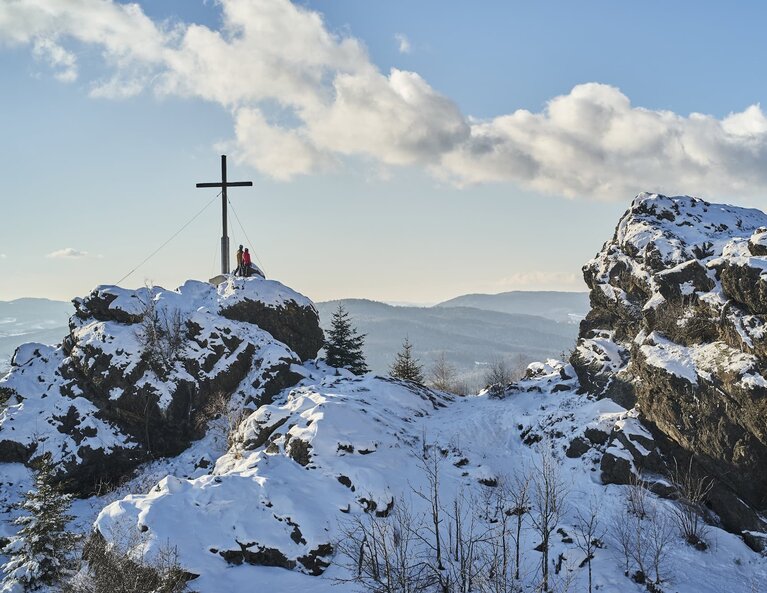 An einem schönen Wintertag stehen zwei Personen am Gipfelkreuz des Silberbergs. | © Bodenmais Tourismus & Marketing GmbH