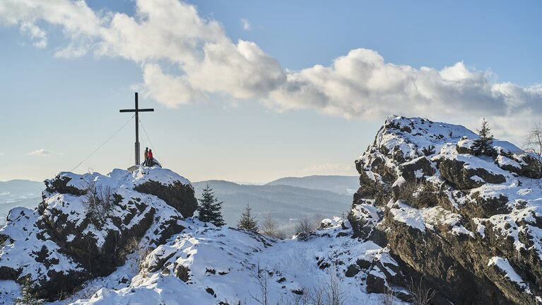 An einem schönen Wintertag stehen zwei Personen am Gipfelkreuz des Silberbergs. | © Bodenmais Tourismus & Marketing GmbH