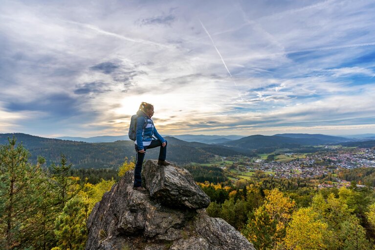 Eine Frau steht auf einem Fels am Silberberg. Ein Bein hat sie vor sich auf eine höhere Stelle gestellt und blickt nach Bodenmais.  | © Bodenmais Tourismus & Marketing GmbH