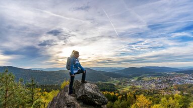 Eine Frau steht auf einem Fels am Silberberg. Ein Bein hat sie vor sich auf eine höhere Stelle gestellt und blickt nach Bodenmais.  | © Bodenmais Tourismus & Marketing GmbH