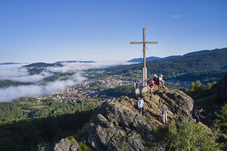 Mehrere Wanderer stehen am Gipfelkreuz des Silberbergs und blicken hinab auf Bodenmais, wo der Nebel hineinkriecht. | © Bodenmais Tourismus & Marketing GmbH